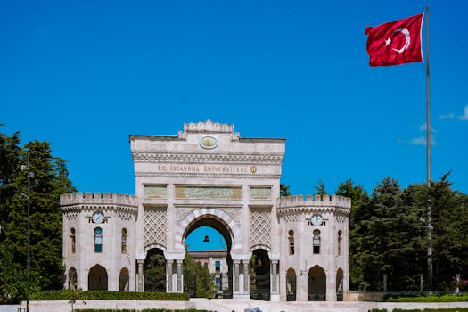 The grand entrance of Istanbul University adorned with a Turkish flag under a clear blue sky.